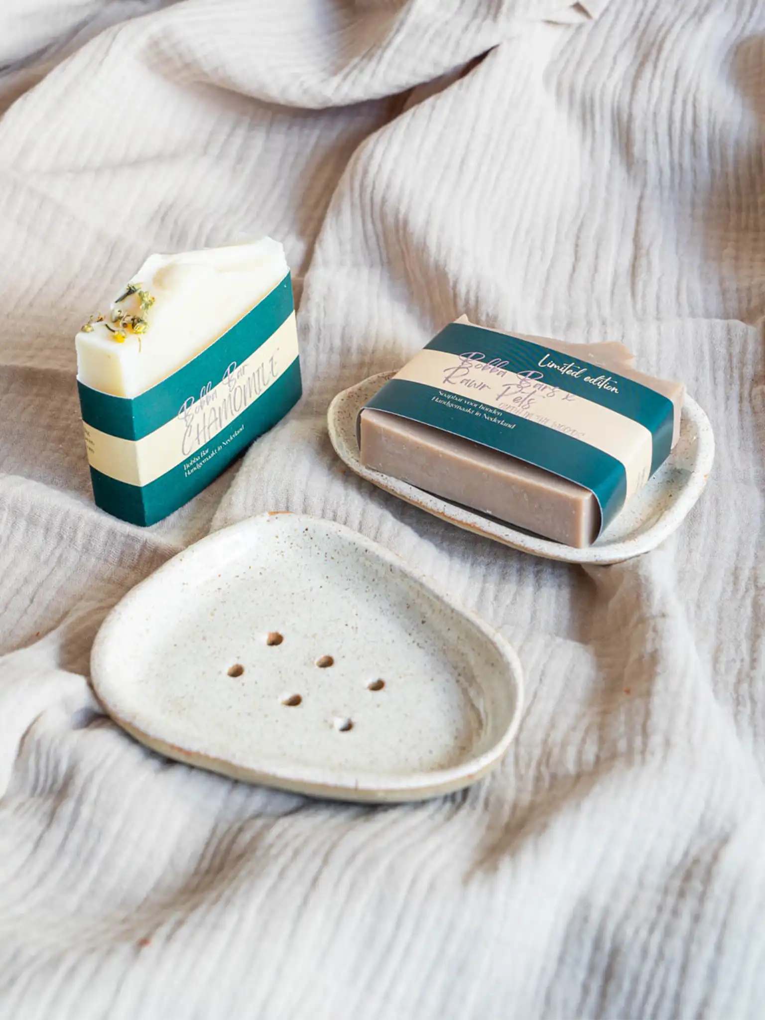 Minimalistisch gespikkeld keramieken zeepschaaltje van Iris Floor, gepresenteerd met handgemaakte Bobba Bars hondenzeep. Het ambachtelijke schaaltje heeft afwateringsgaatjes voor een duurzaam gebruik.