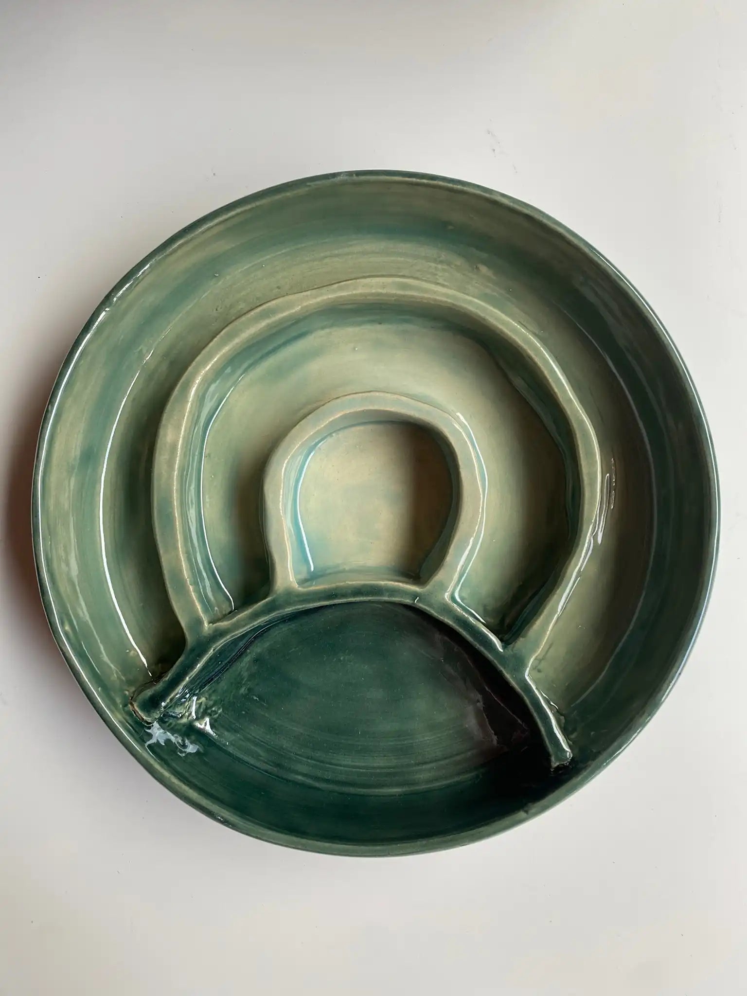 Handgemaakte keramieken hondenbak set van Iris Floor in mosgroen glazuur. De set bevat een functionele slowfeeder met brokken en een bijpassende drinkbak op een houten vloer.