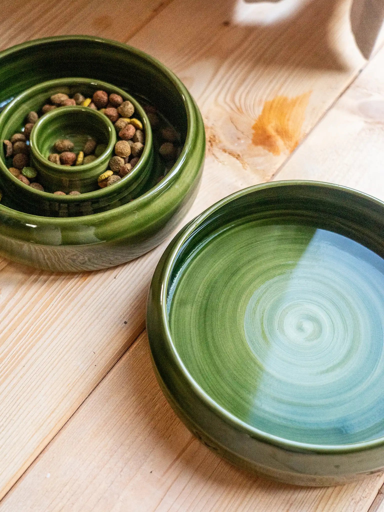 Set van twee handgemaakte keramieken hondenbakken door Iris Floor in mosgroen glazuur. Bevat een unieke keramieken slowfeeder voerbak en een bijpassende drinkbak op een houten vloer.