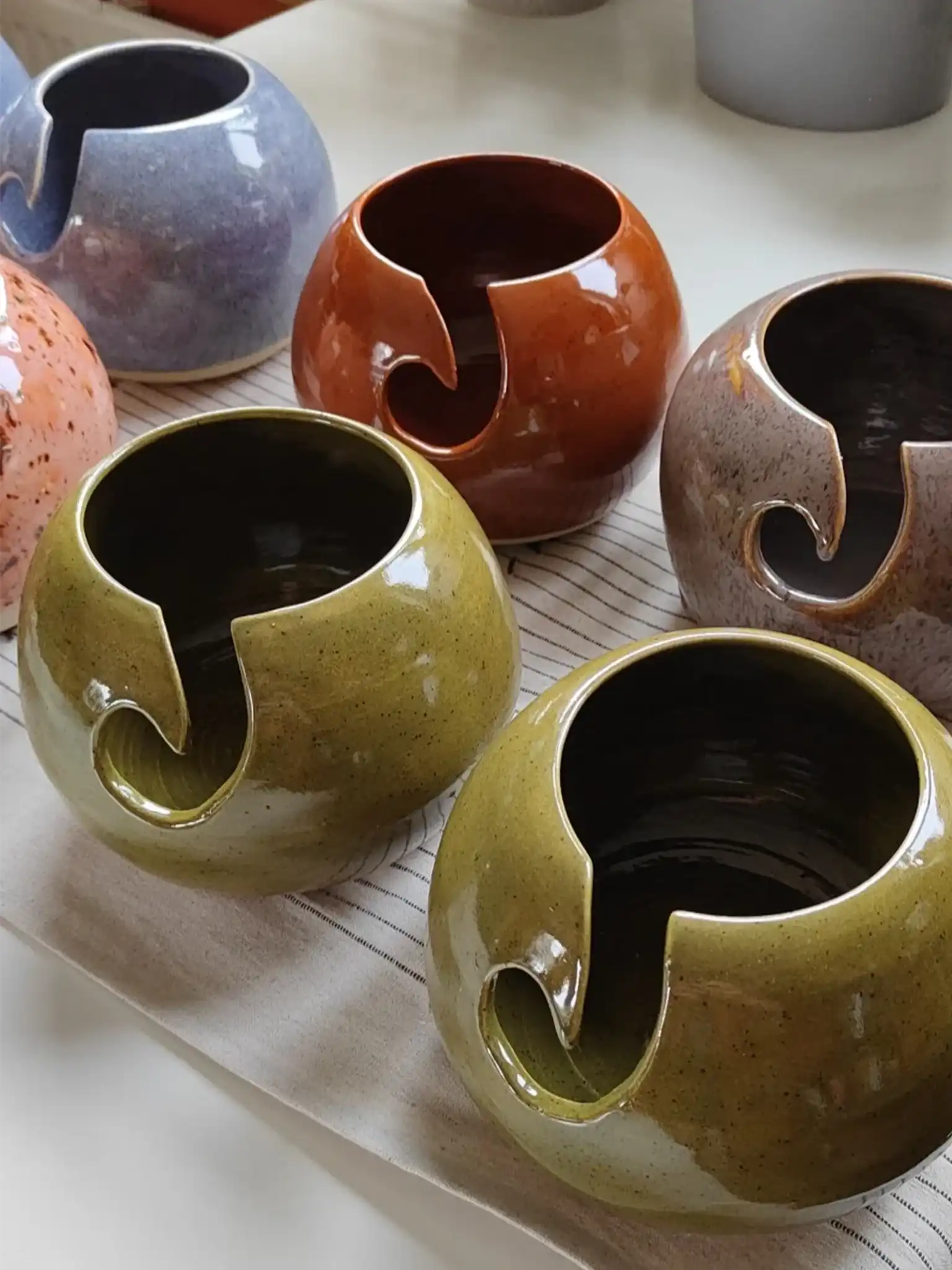 Handgemaakte keramieken yarn bowl door Iris Floor voor een 100g cake wol. Deze ambachtelijke wolkom, beschikbaar in kleuren als Deep Olive en Amaryllis, is uniek gedraaid in Nederland en voorzien van een gladde uitsparing voor het garen.