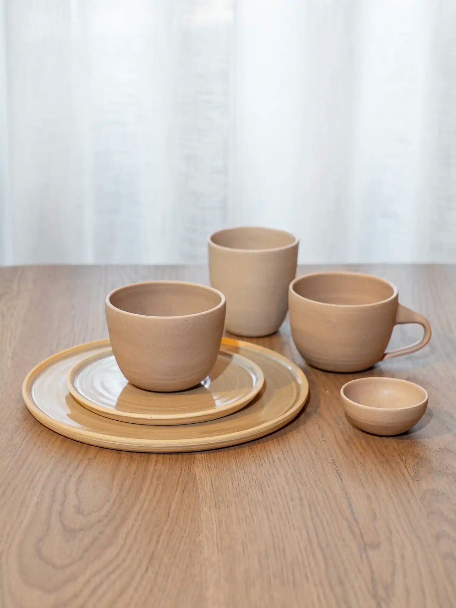 Handgemaakt keramiek high tea servies in zandtinten — beker, mok, bord en klein schaaltje op houten tafel — Iris Floor Ceramics`