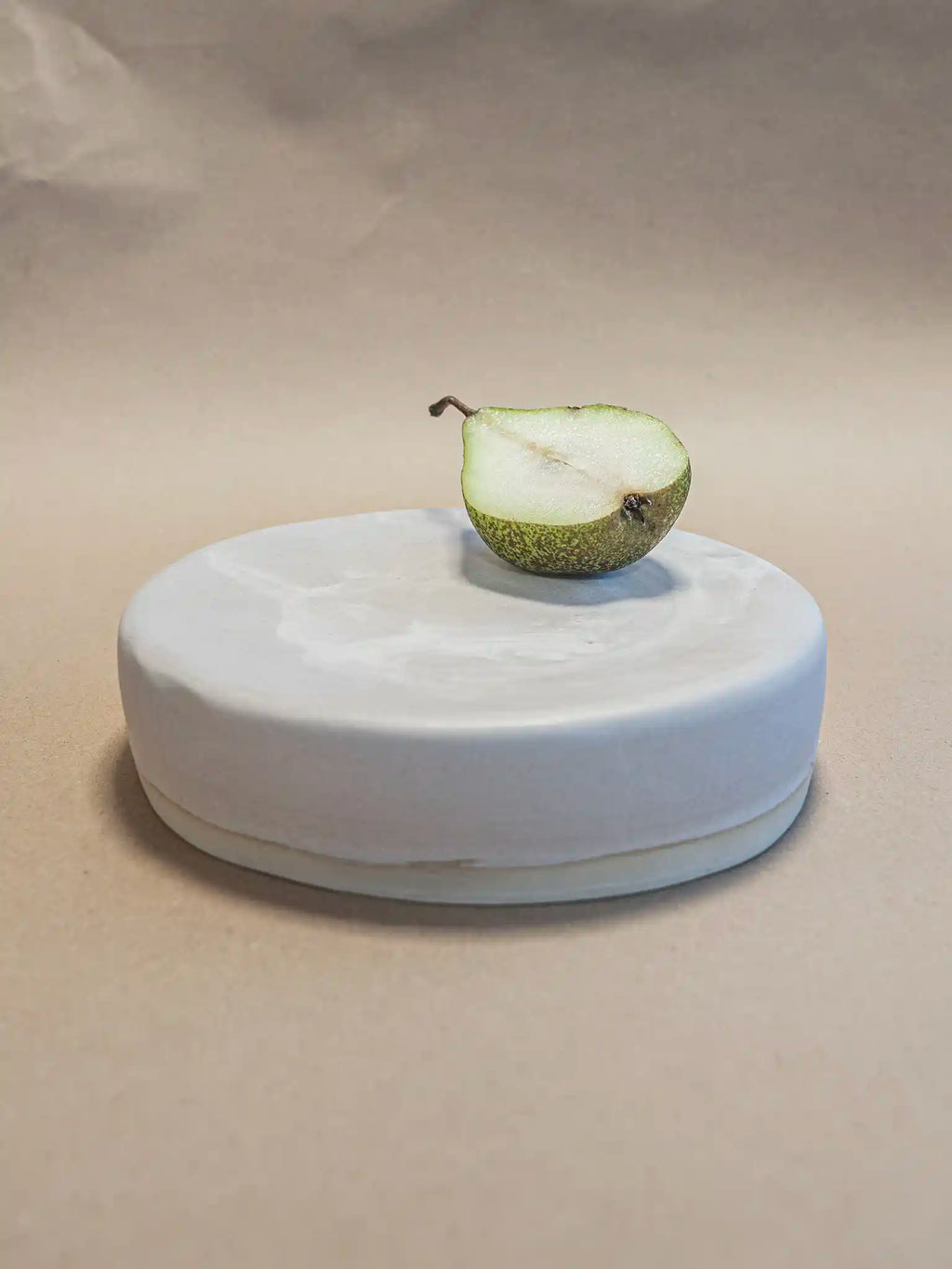 Handgemaakt keramiek serveerplateau in mat marmer glazuur met een halve peer als styling, zijaanzicht op beige achtergrond — Iris Floor Ceramics
