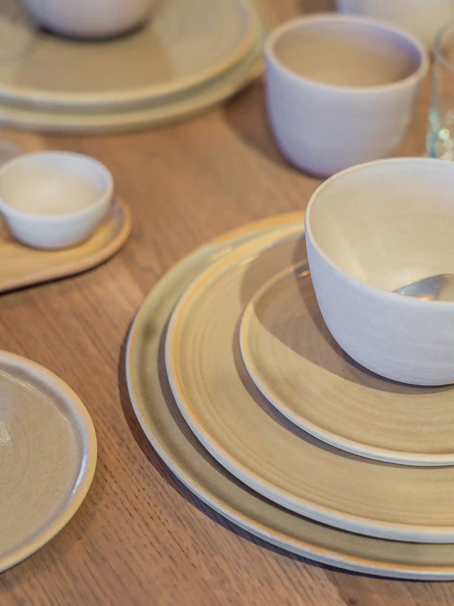 Gedekte tafel met handgemaakte keramieken borden, kommen en schaaltjes in wit en zandtinten op een houten tafel — Iris Floor Ceramics