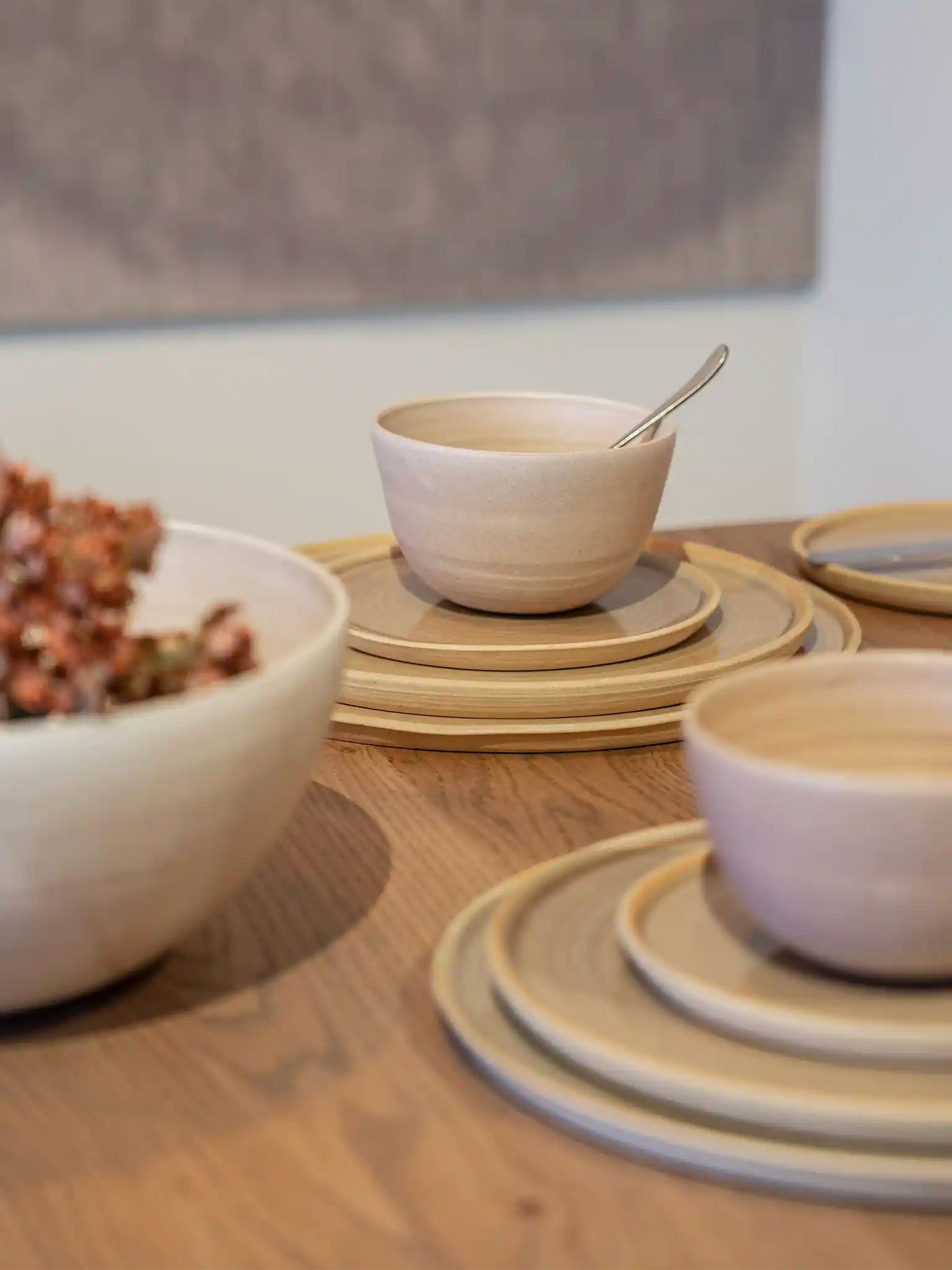 Handgemaakte keramieken kommen op gestapelde borden in gebruik tijdens een maaltijd, zandkleurig glazuur op houten tafel — Iris Floor Ceramics