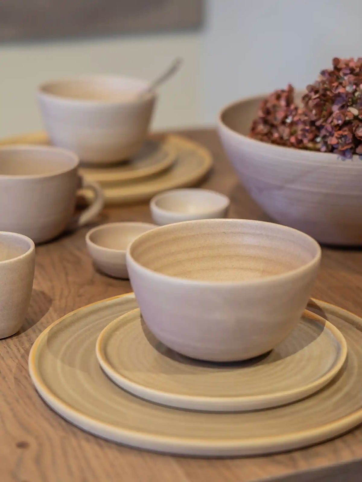 Handgemaakte keramieken kom op gestapelde borden in zandtinten, gestyled met gedroogde hortensia's op een houten tafel — Iris Floor Ceramics
