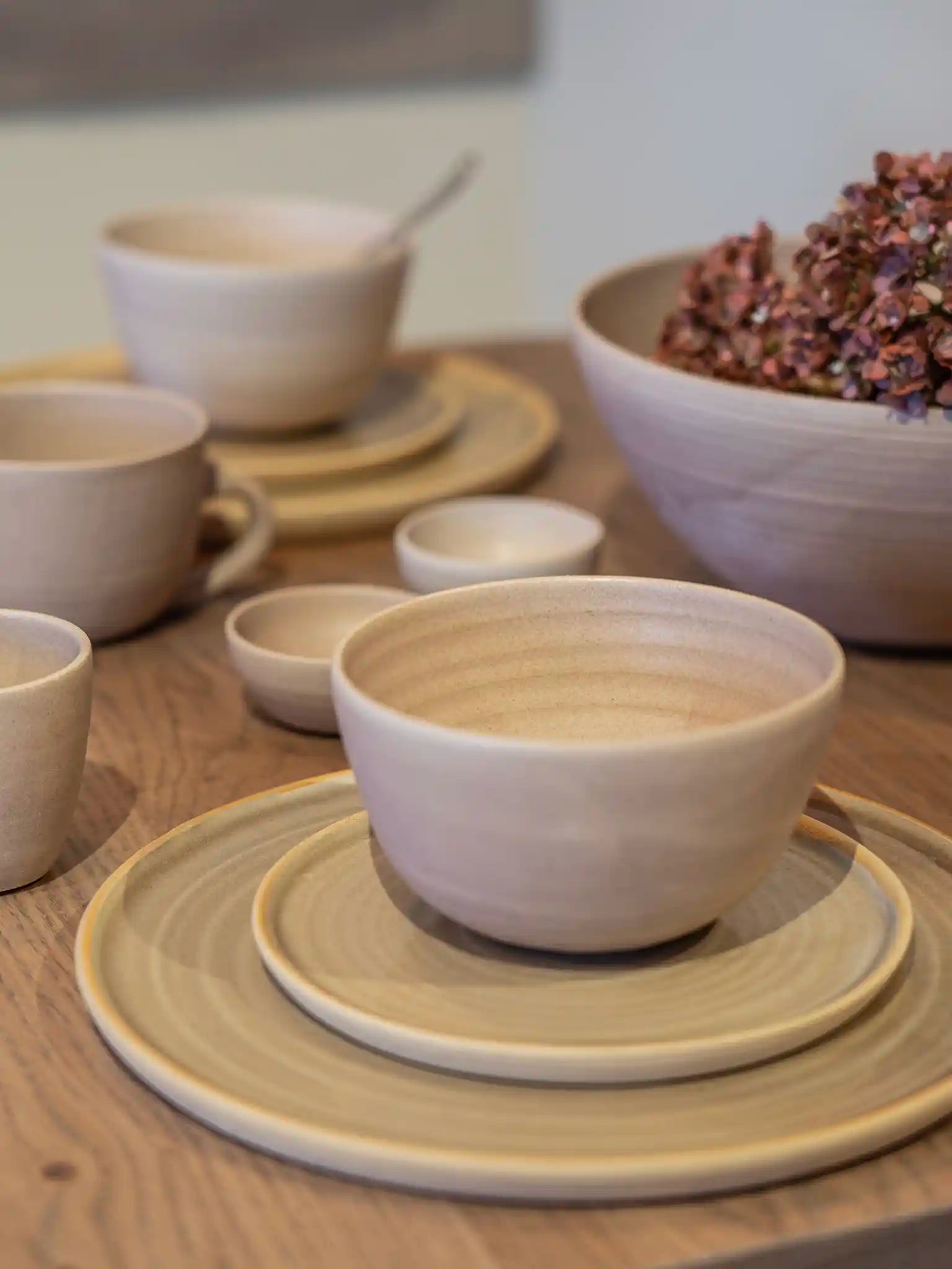 Handgemaakte keramieken kom op gestapelde borden in zandtinten, gestyled met gedroogde hortensia's op een houten tafel — Iris Floor Ceramics
