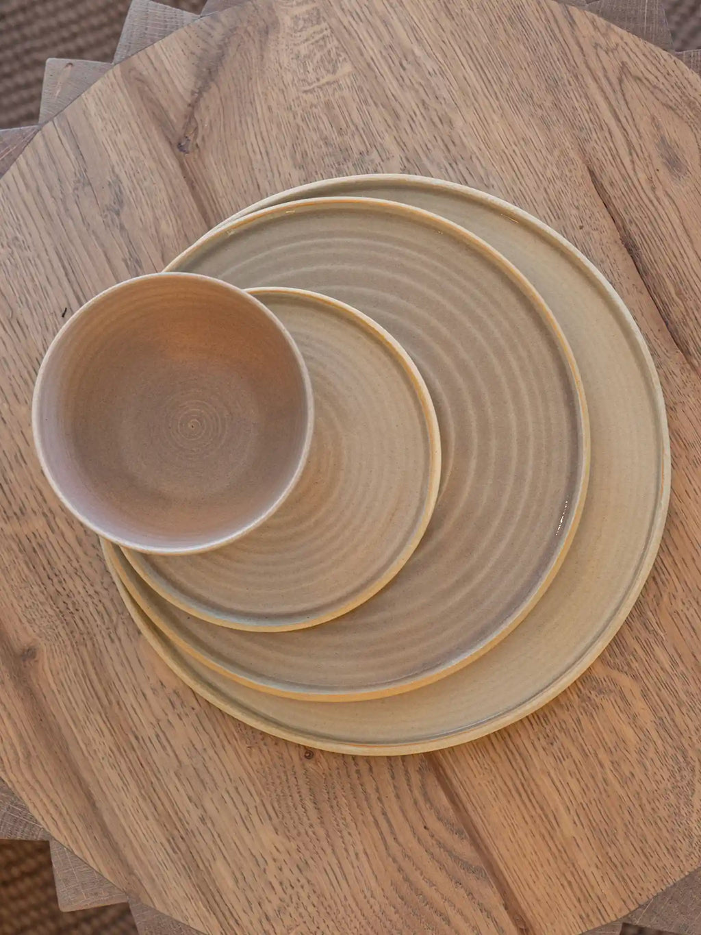 Handgemaakte keramieken borden en schaaltje in drie maten gestapeld, zandkleurig glazuur met draailijnen, bovenaanzicht — Iris Floor Ceramics