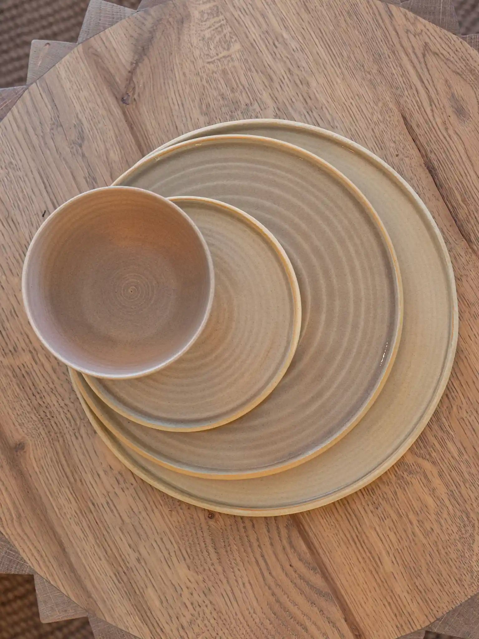 Handgemaakte keramieken borden en schaaltje in drie maten gestapeld, zandkleurig glazuur met draailijnen, bovenaanzicht — Iris Floor Ceramics
