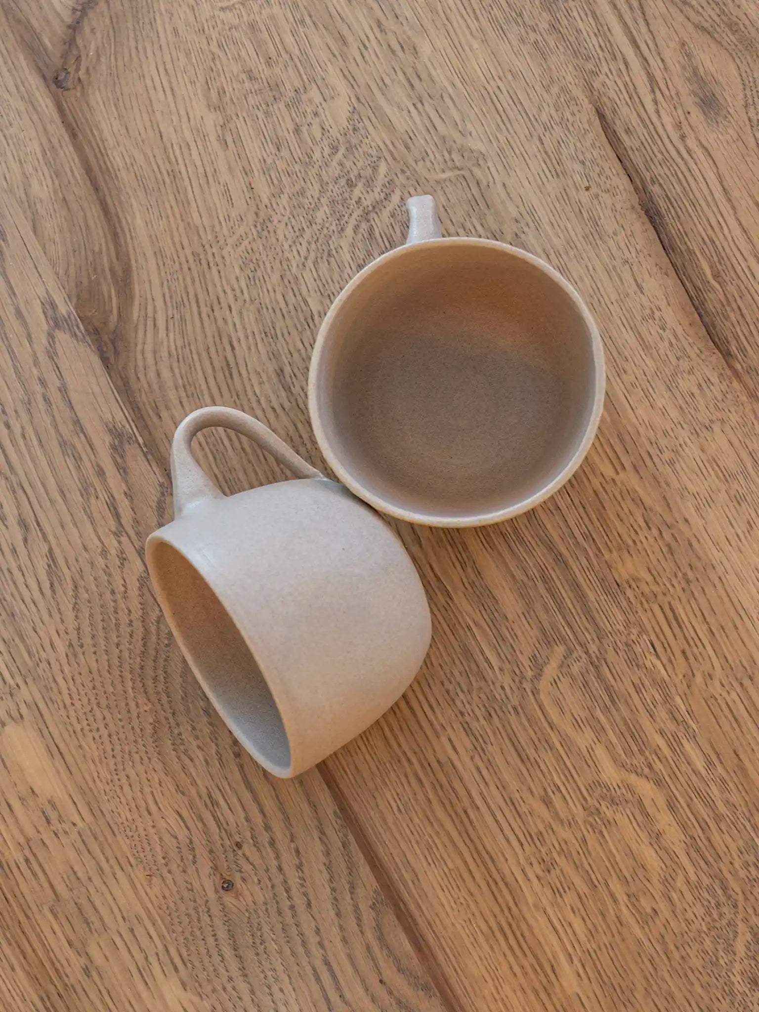 Twee handgemaakte keramieken mokken in zandtinten op een houten tafel, bovenaanzicht — Iris Floor Ceramics
