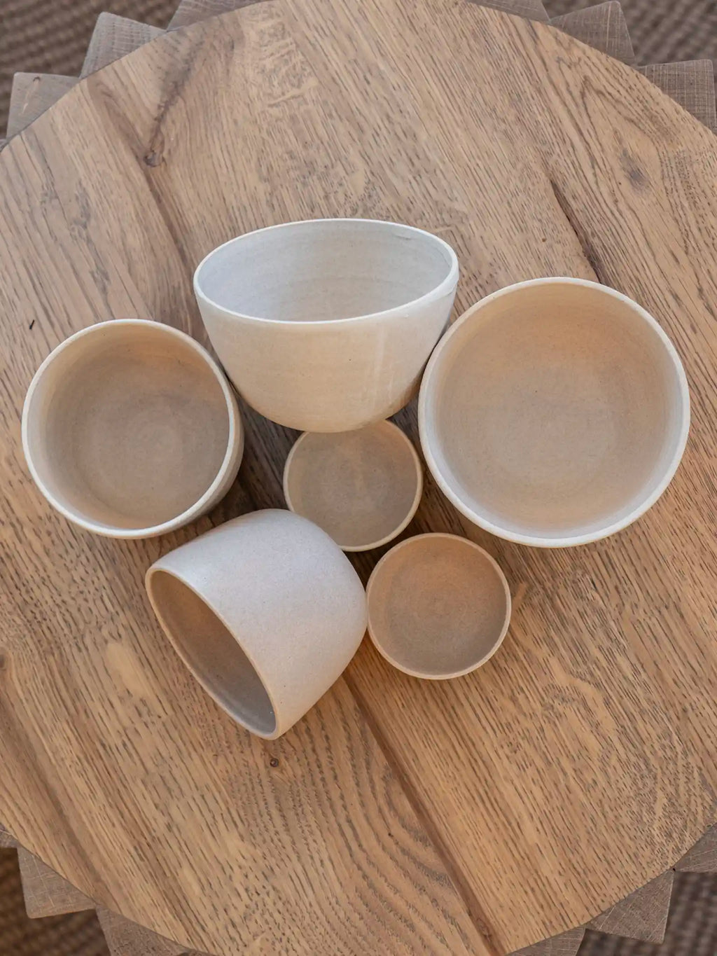Handgemaakte keramieken kommen en schaaltjes in verschillende maten en vormen, zand- en wittinten, bovenaanzicht op houten tafel — Iris Floor Ceramics